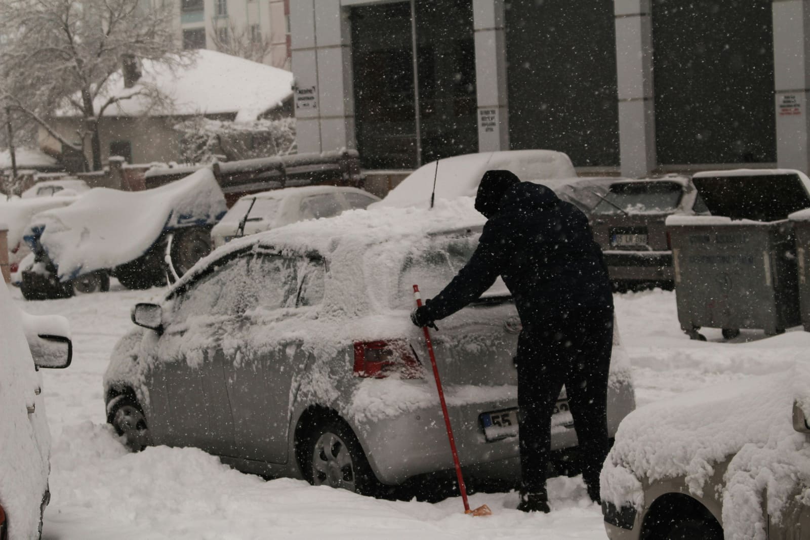 Person cleaning snow off car during Chicago winter - proper winter car preparation and maintenance
